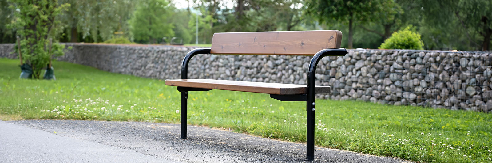 Wooden park bench with a backrest and black frame and armrests on a public walkway.